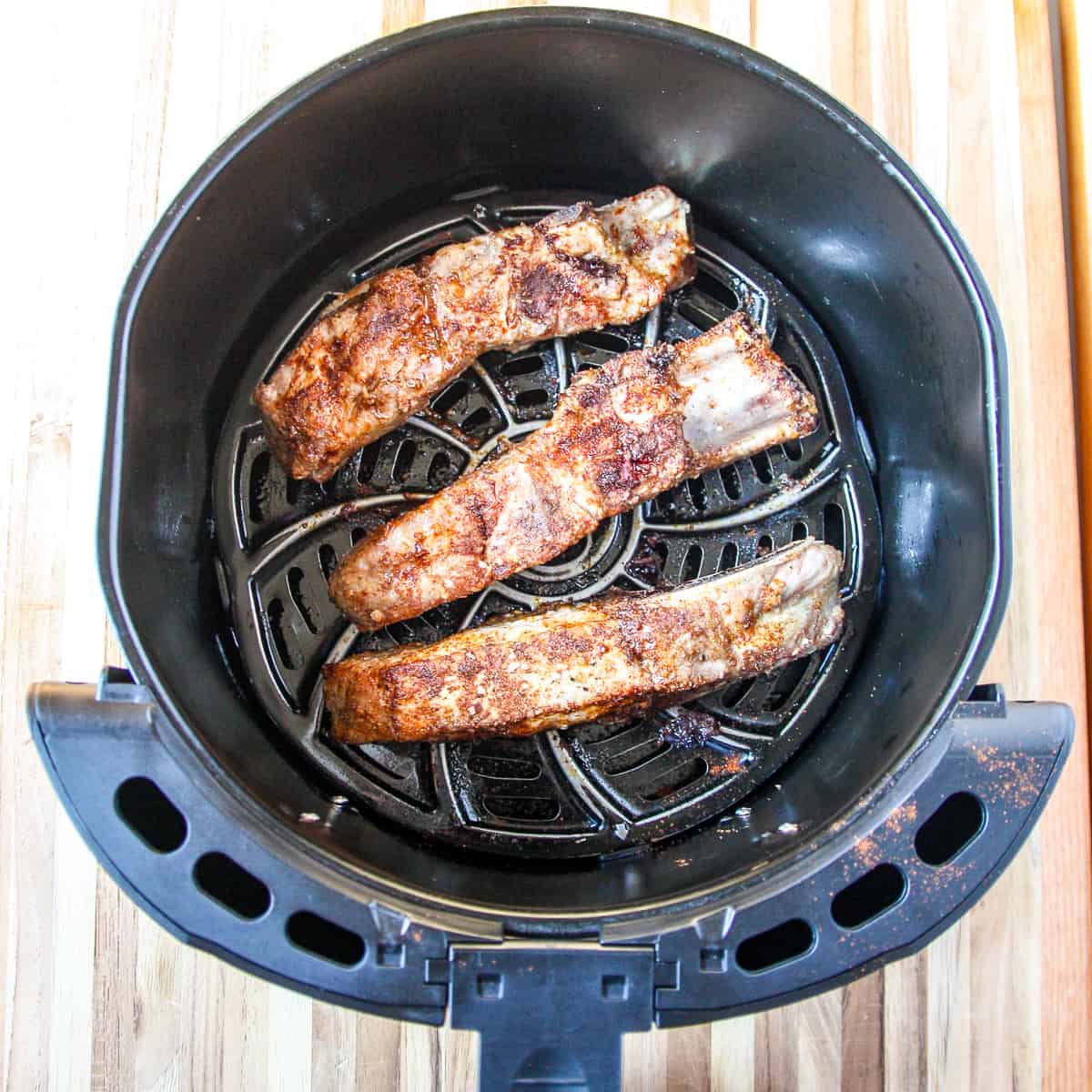 Partially cooked pork ribs in an air fryer basket.
