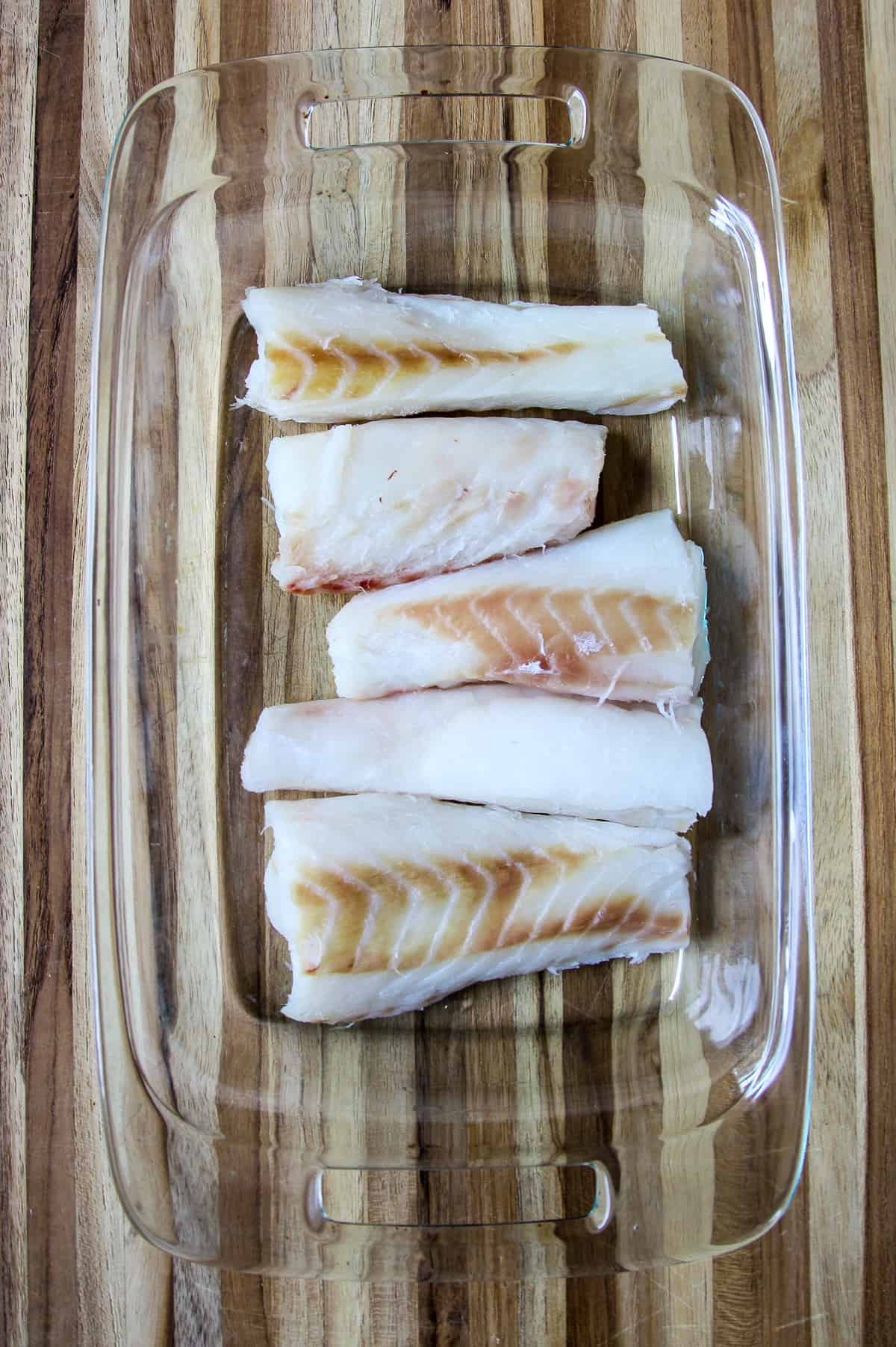 Uncooked cod loins in a glass pan.