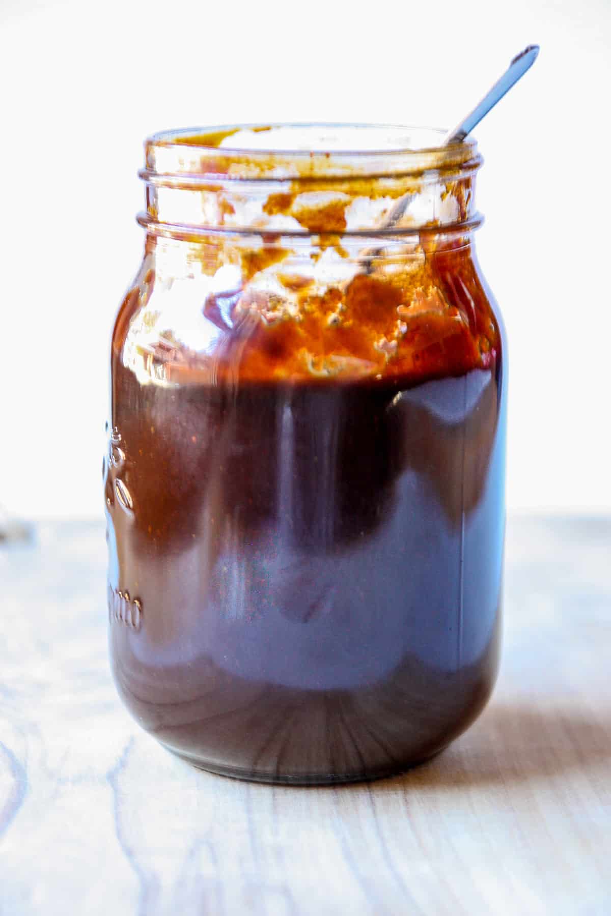 A jar half full of BBQ sauce with a spoon in it.