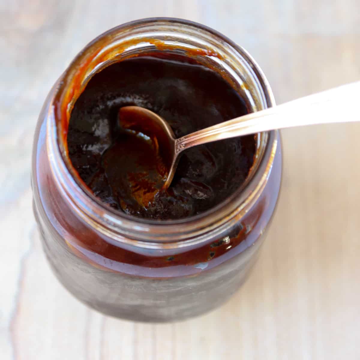 A silver spoon dipping into a jar of barbecue sauce.