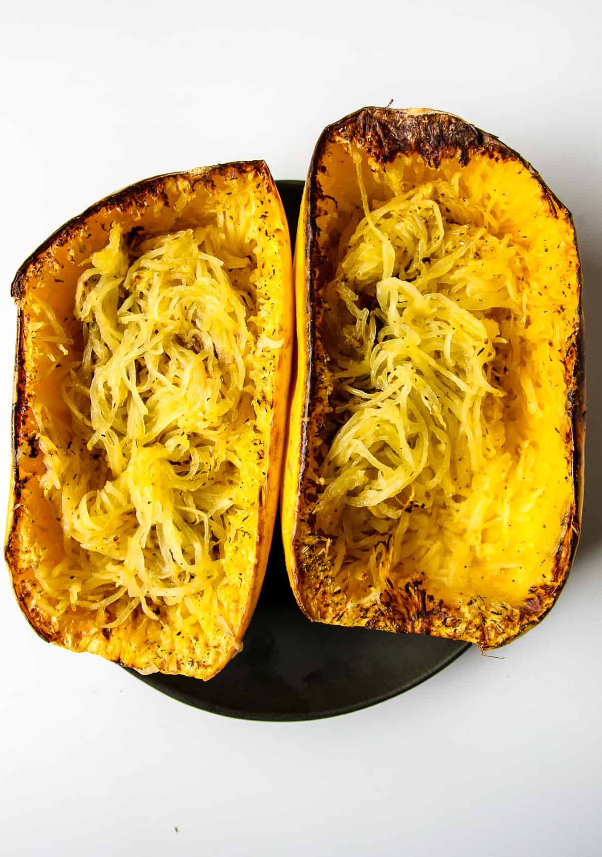 Two air fried halves of spaghetti squash on a black plate.
