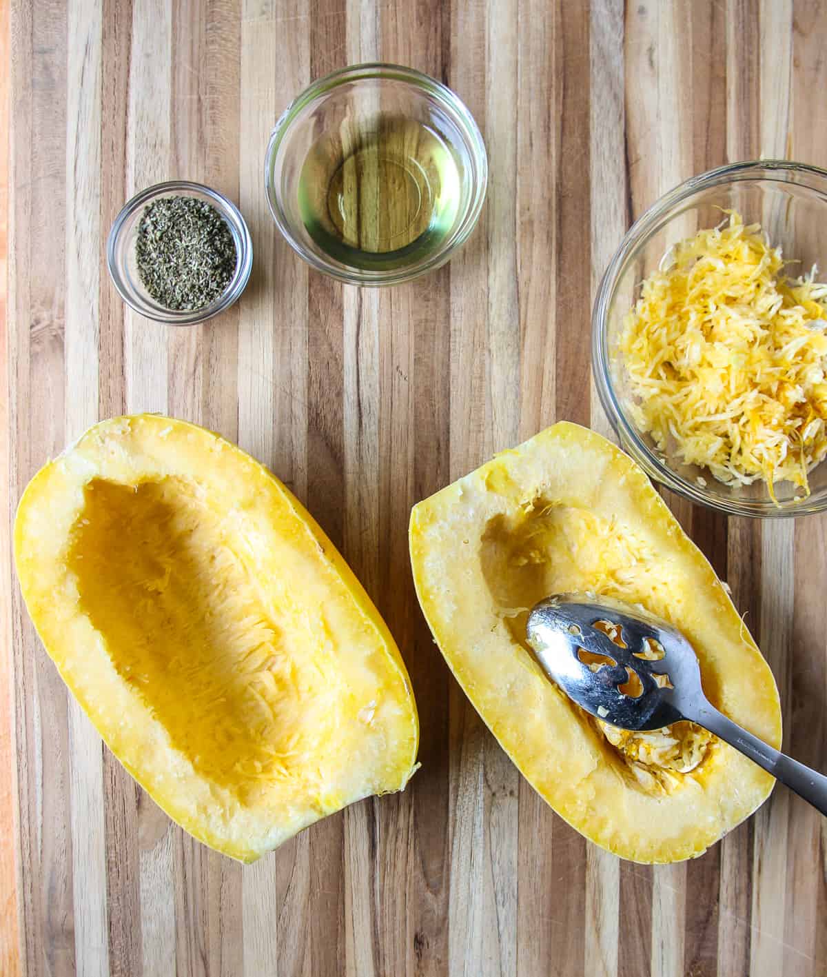A spoon being used to scoop out the seeds from the squash halves.