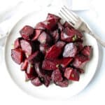 Cubed roasted red beets on a white plate with a silver fork.