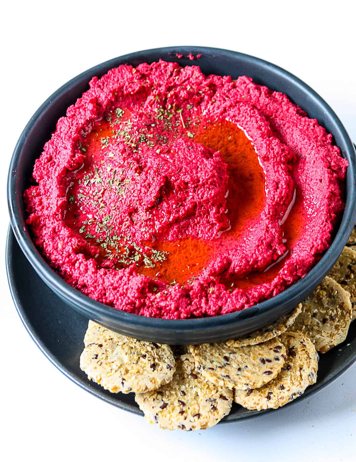 A bowl of beet hummus surrounded by crackers.