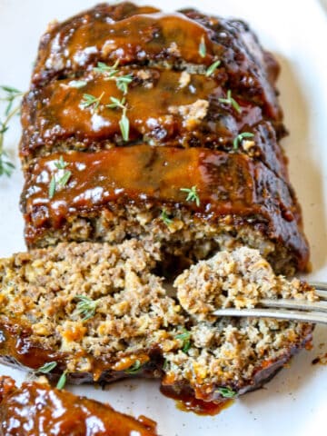 Sliced air fryer meatloaf on a white plate with a fork taking a piece of one slice.
