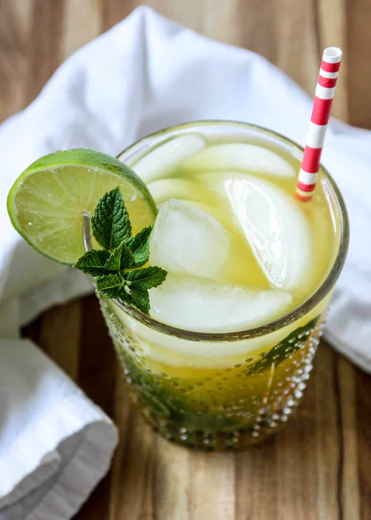 A mango mojito in a clear bubble patterned glass garnished with mint and lime.