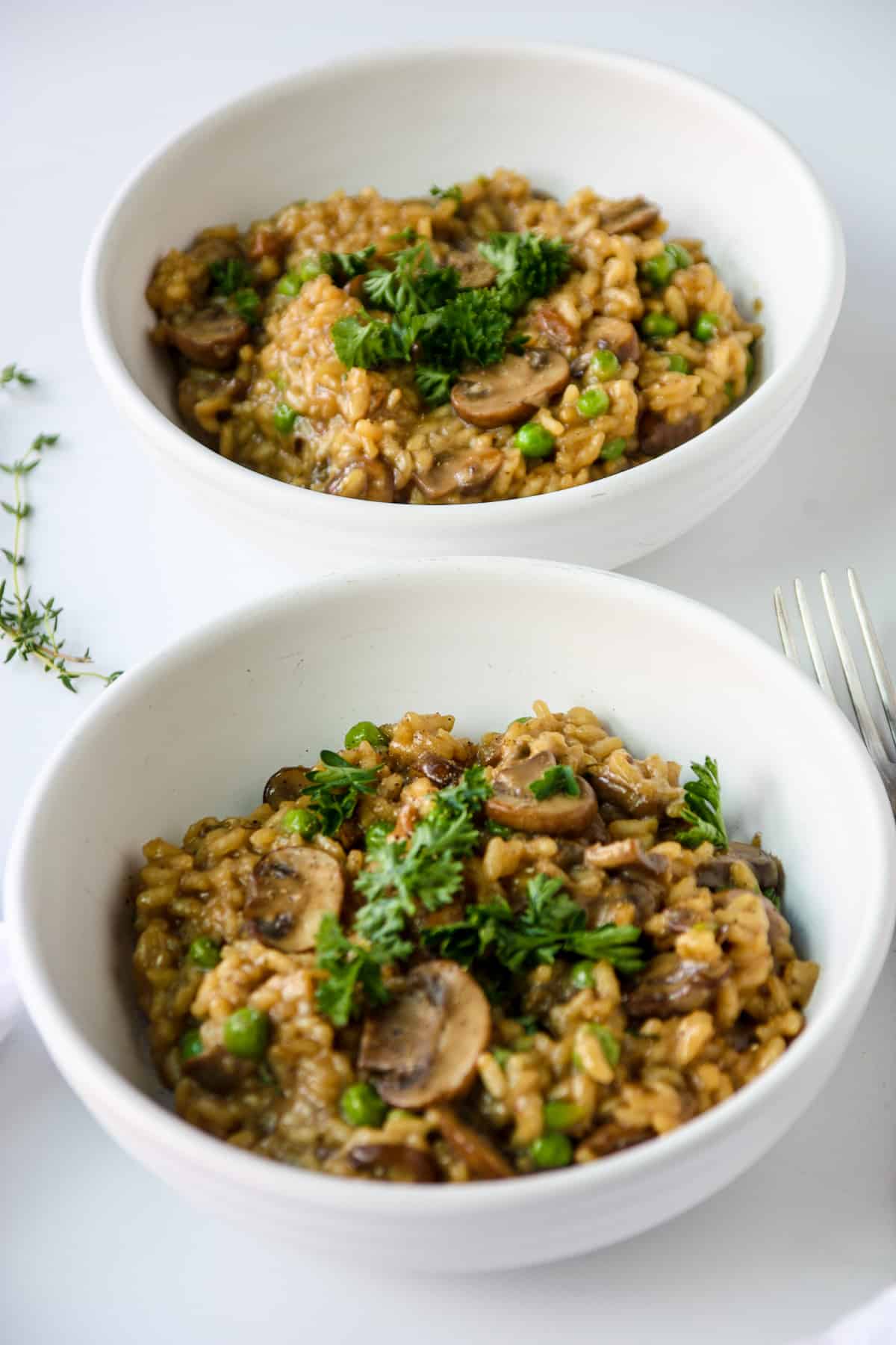 Two white bowls of mushroom pea risotto.
