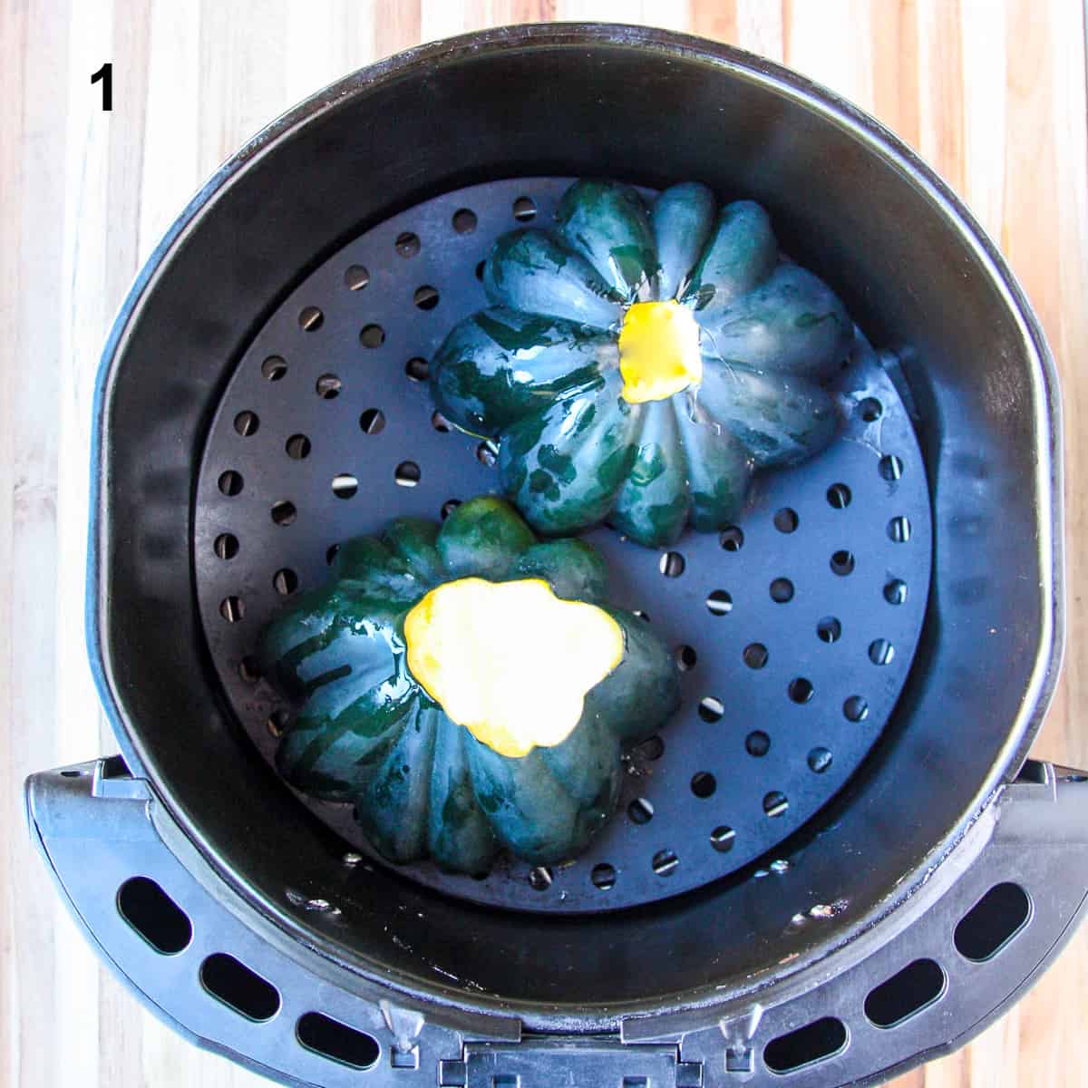Two acorn squash halves cut side down in an air fryer basket.