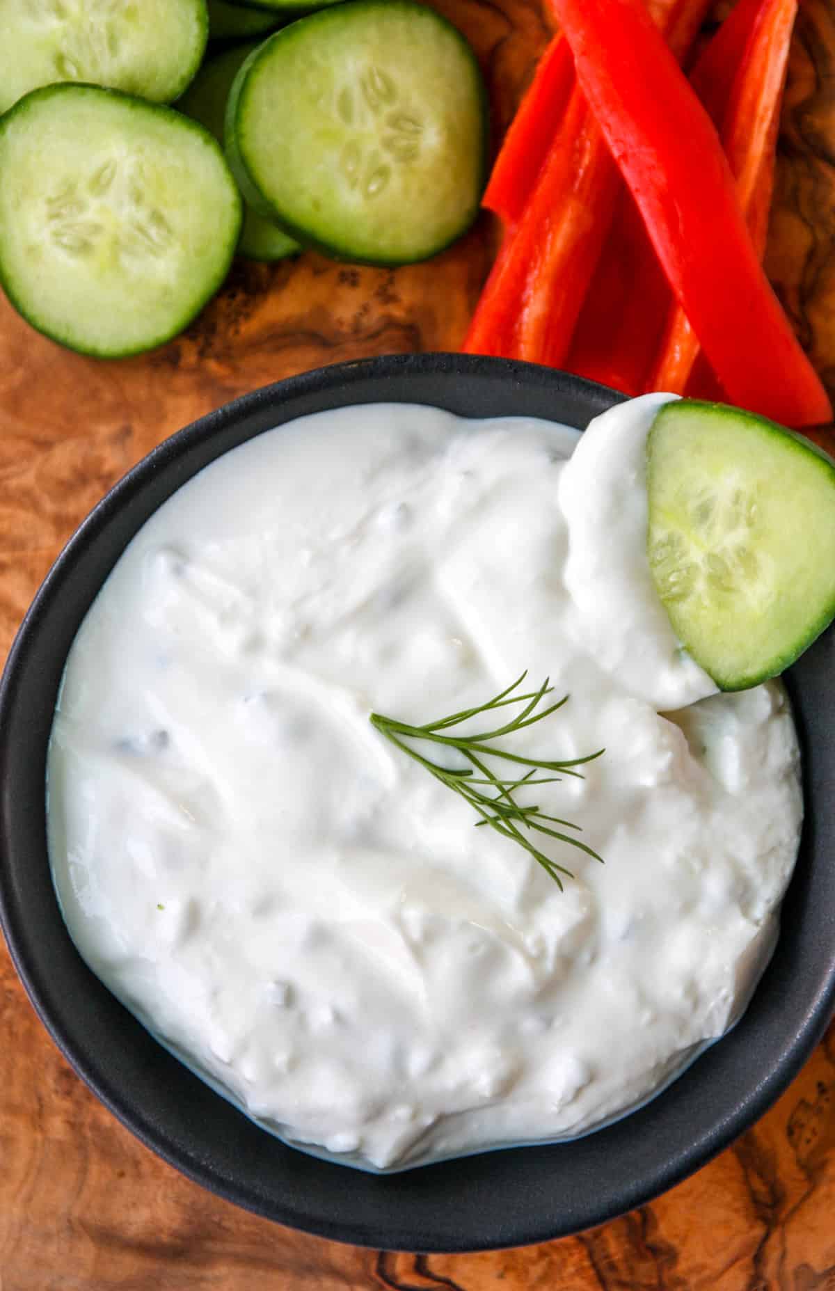 A cucumber slice being dipped into a bowl of tzatziki.