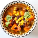 Sweet potato soup with black beans and corn in a black and white bowl.
