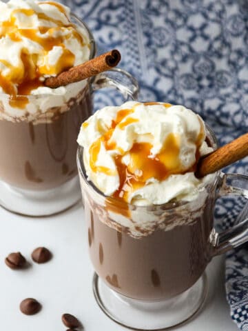 Two glass mugs with Rumchata hot chocolate, topped with whipped cream.