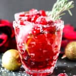 A cranberry mistletoe margarita in a glass with a sprig of rosemary.