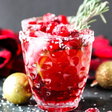 A cranberry mistletoe margarita in a glass with a sprig of rosemary.