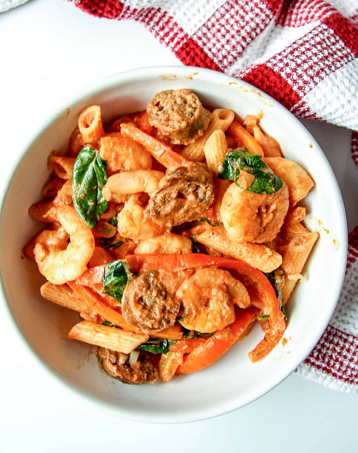 Penne pasta with shrimp, sausage and red peppers in a white bowl.