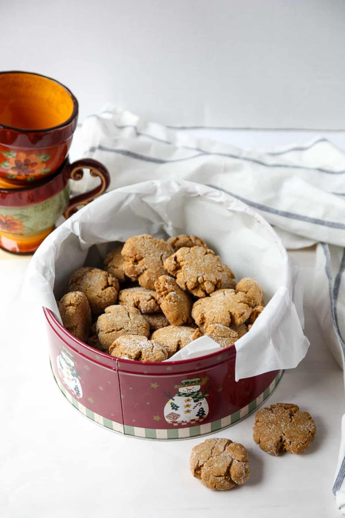A red, snowman decorated cookie tin filled with cookies.