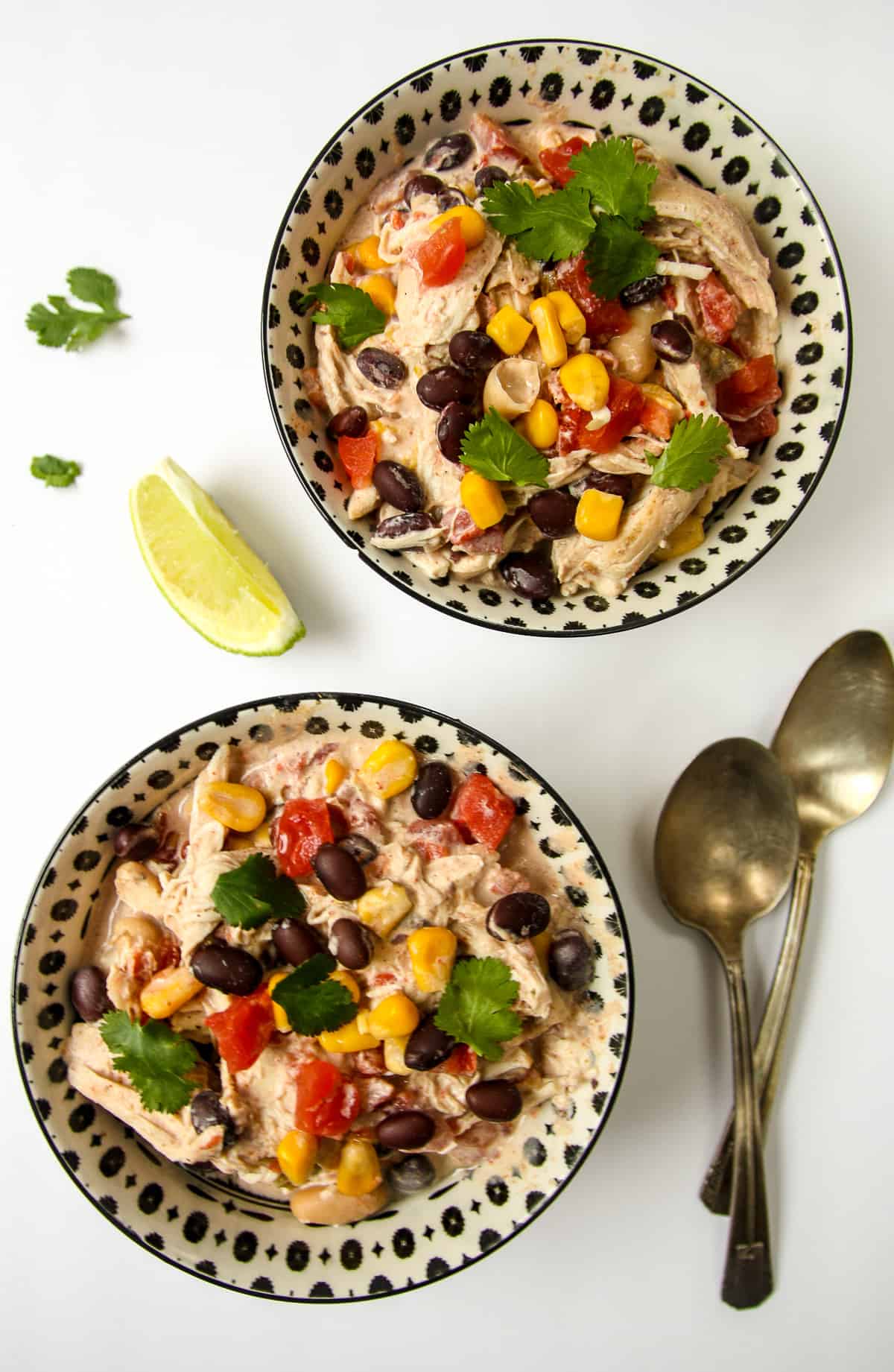 Two servings of chicken chili with two spoons and a lime wedge.