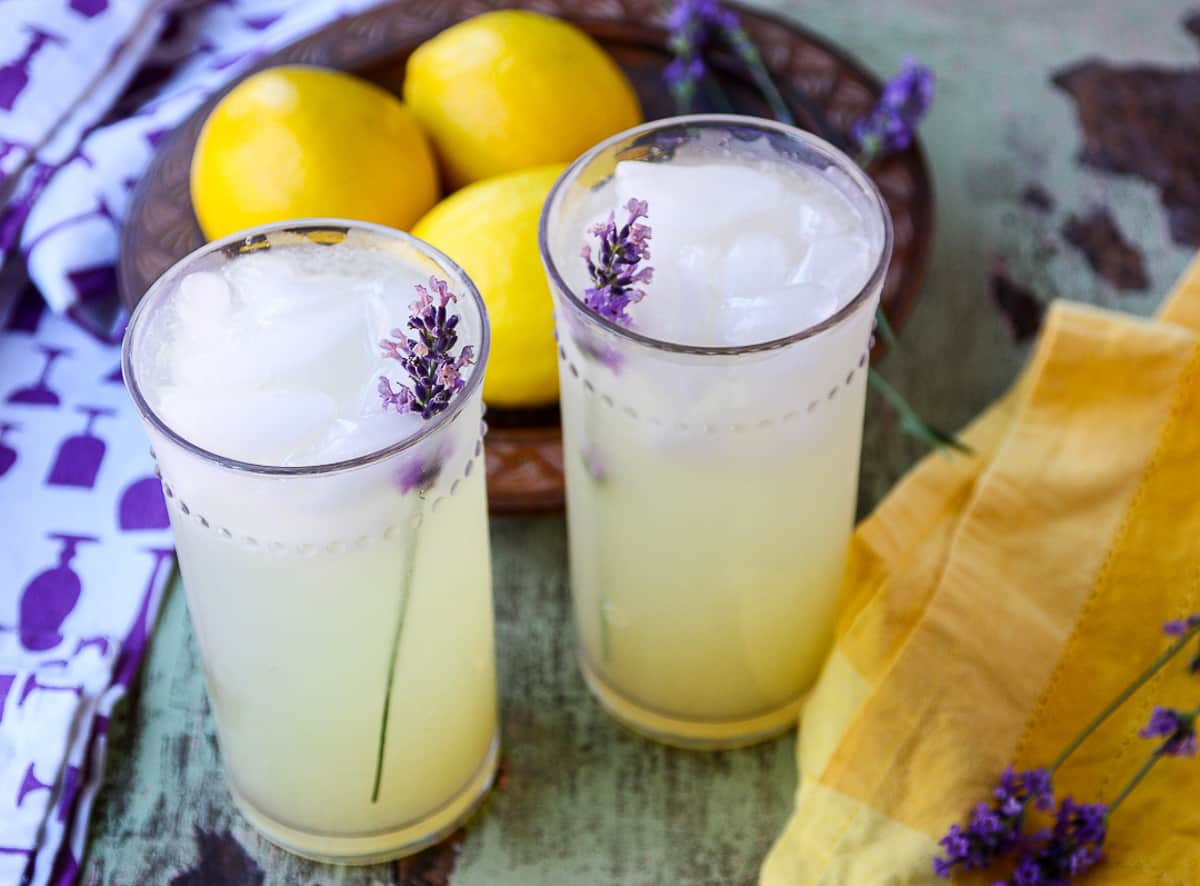 A bowl of lemons and glasses of lemonade of a green table.