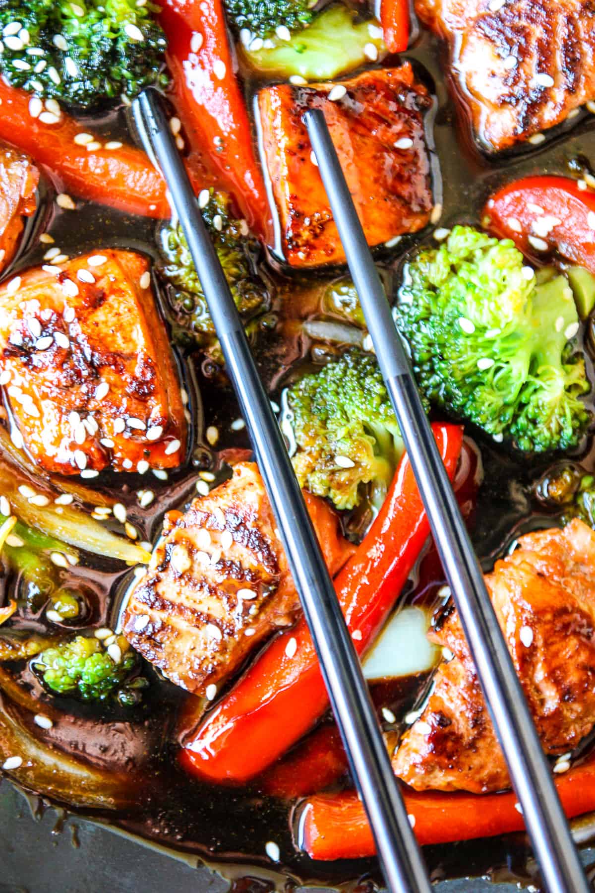 Salmon and vegetables in teriyaki sauce with black chopsticks.