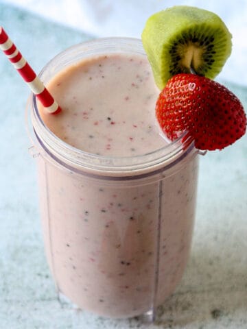 Kiwi quencher tropical smoothie in a tall glass with a pink and white straw.