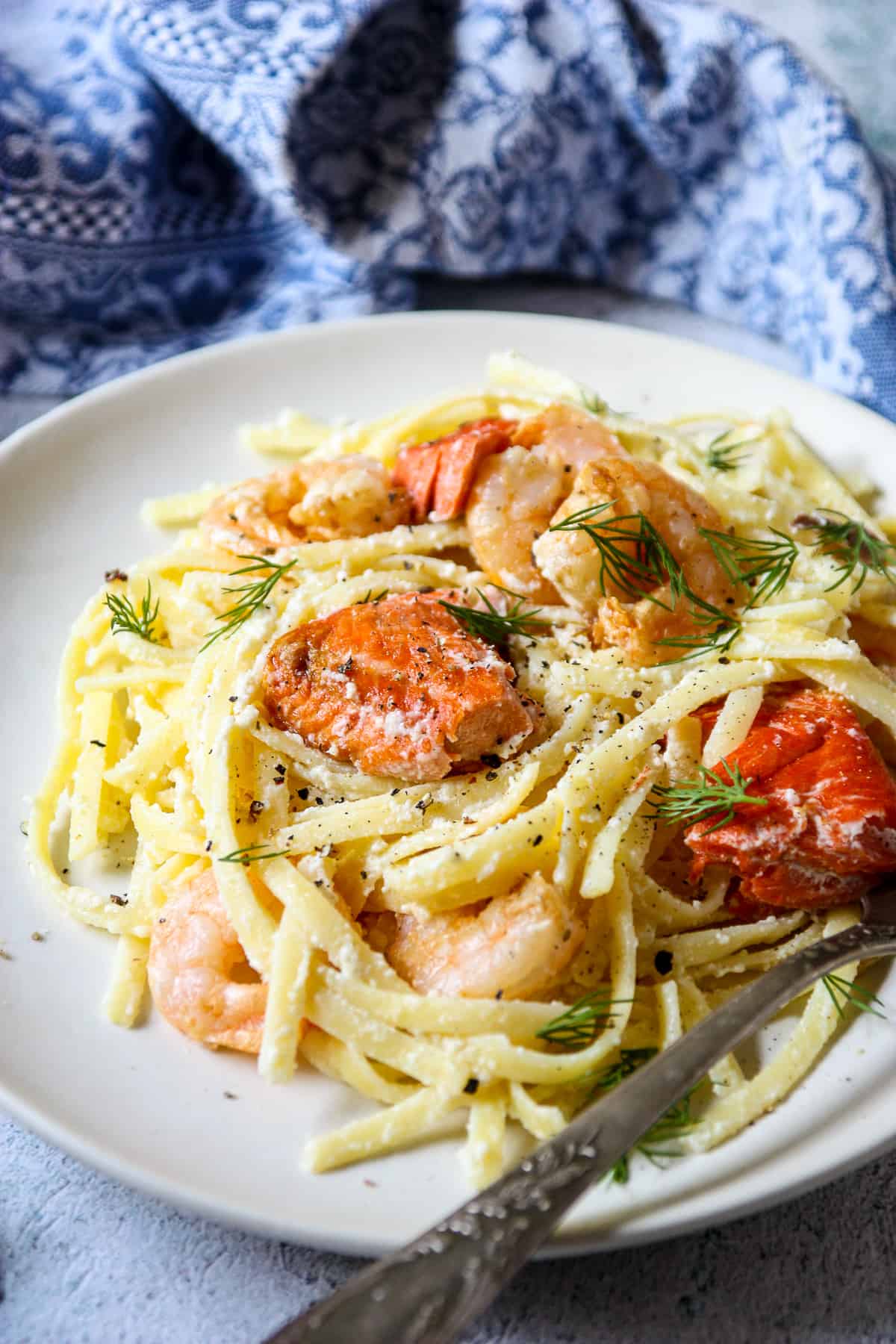 Salmon and shrimp nestled in creamy noodles on a white plate.