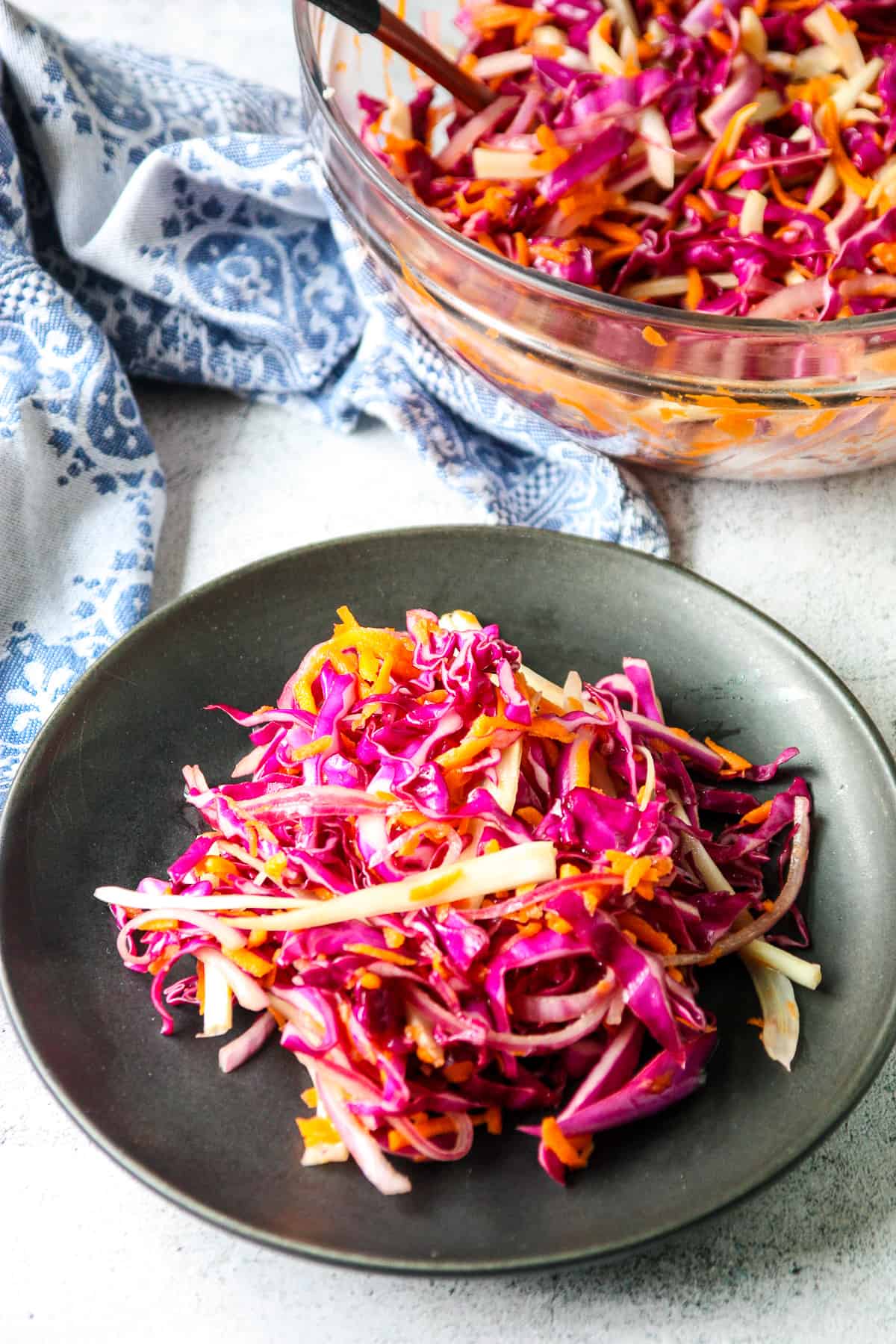 A black plate of red cabbage slaw, next to a glass bowl filled with salad.