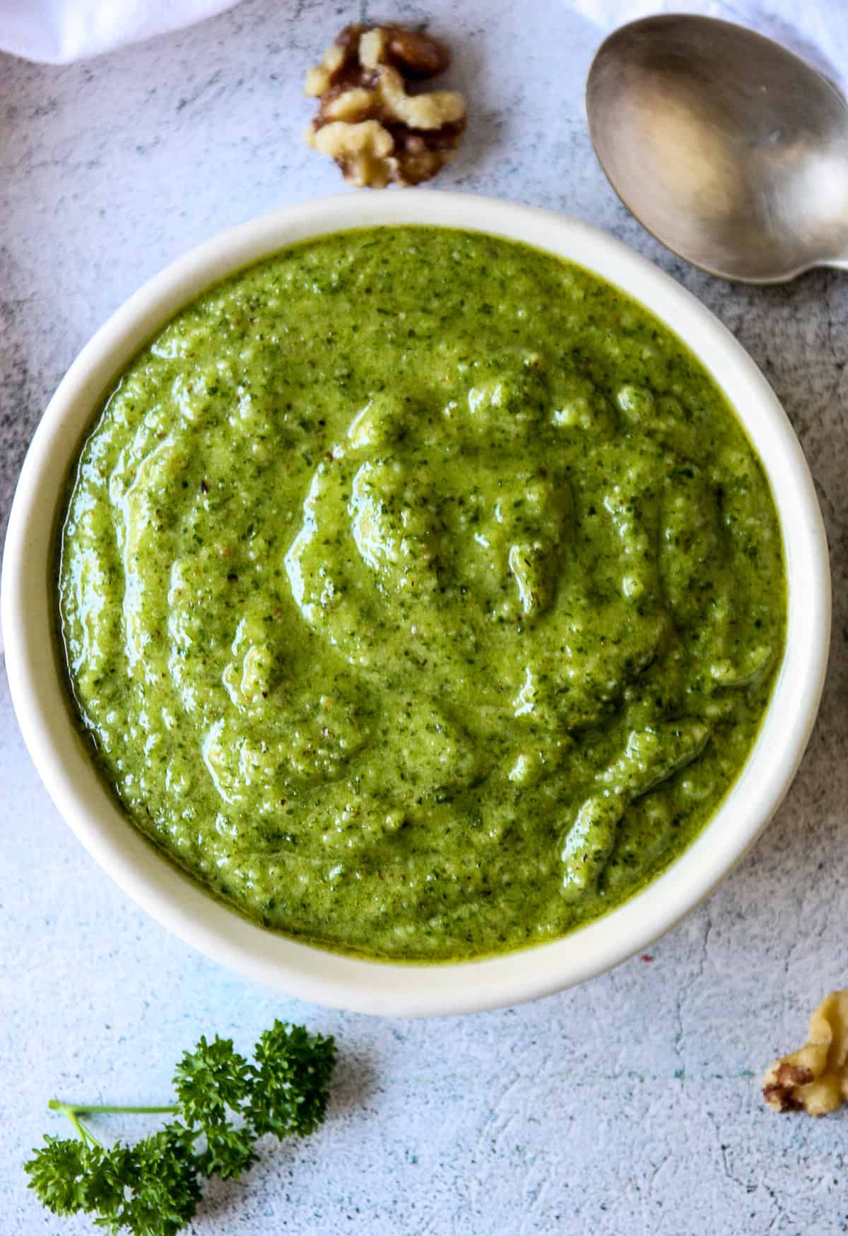 Parsley pesto in a white dish next to a silver spoon.