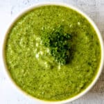 Bright green parsley pesto in a white bowl, garnished with a sprig of fresh parsley.