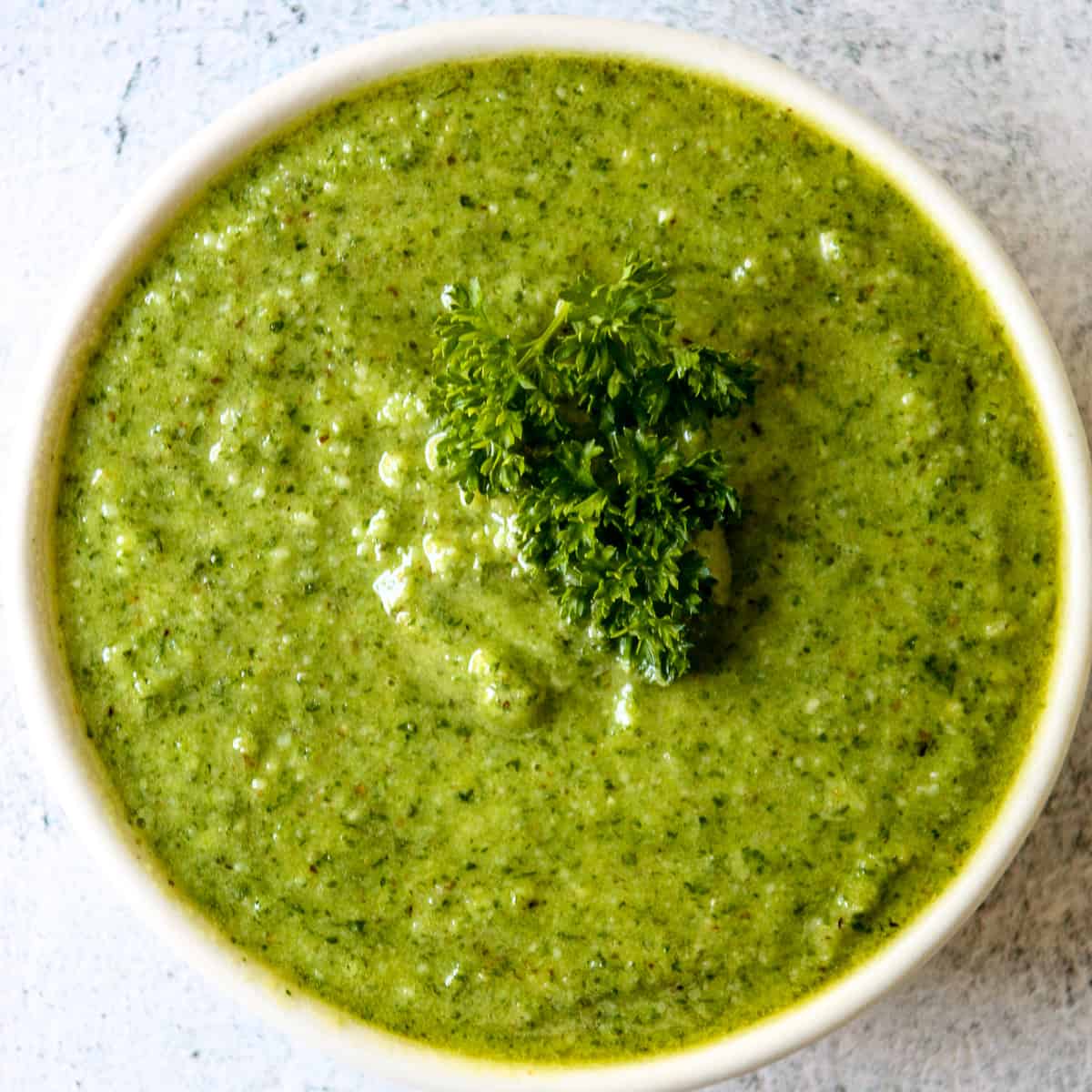 Bright green parsley pesto in a white dish, garnished with a sprig of parsley.