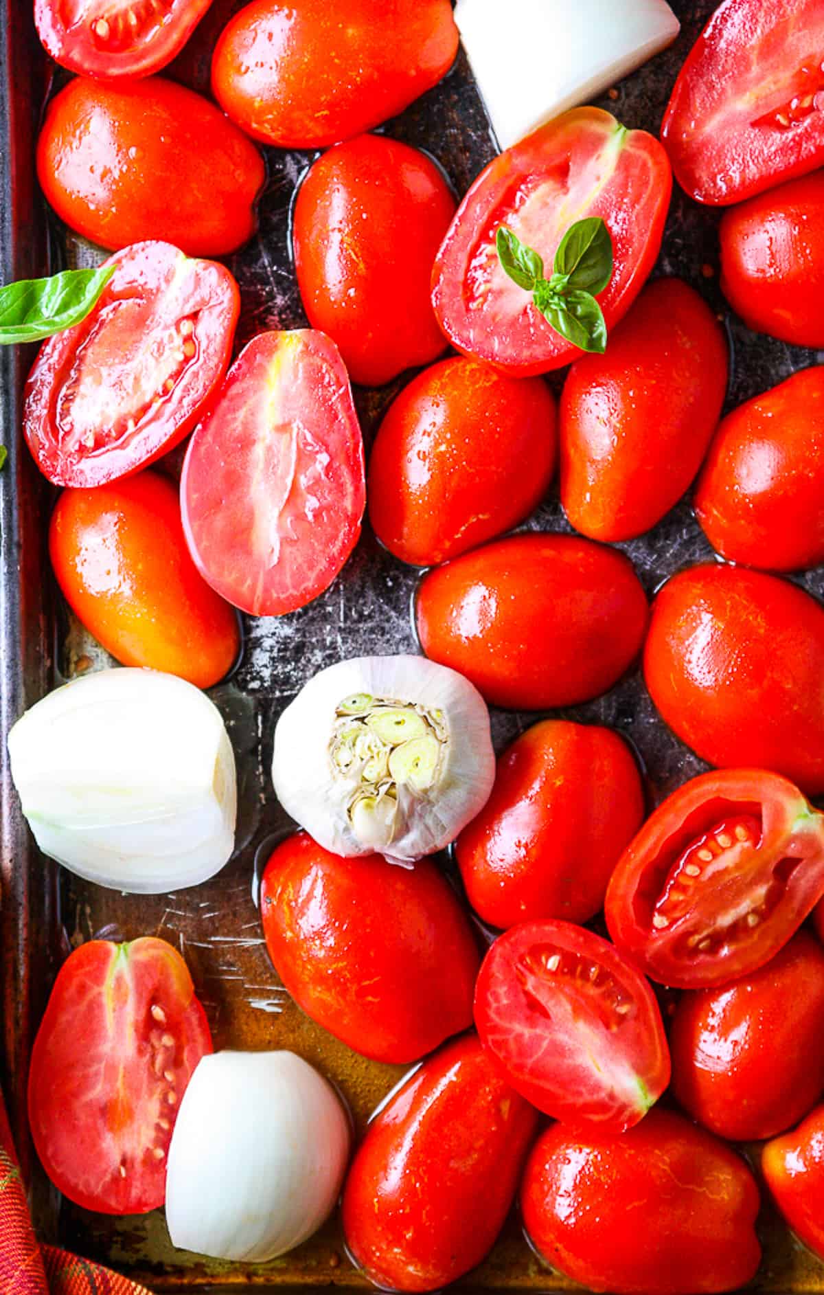 Fresh tomatoes, onions, and garlic on a baking sheet.