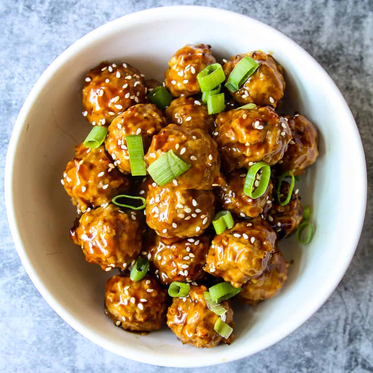 Asian chicken meatballs in a white bowl on a marble countertop.