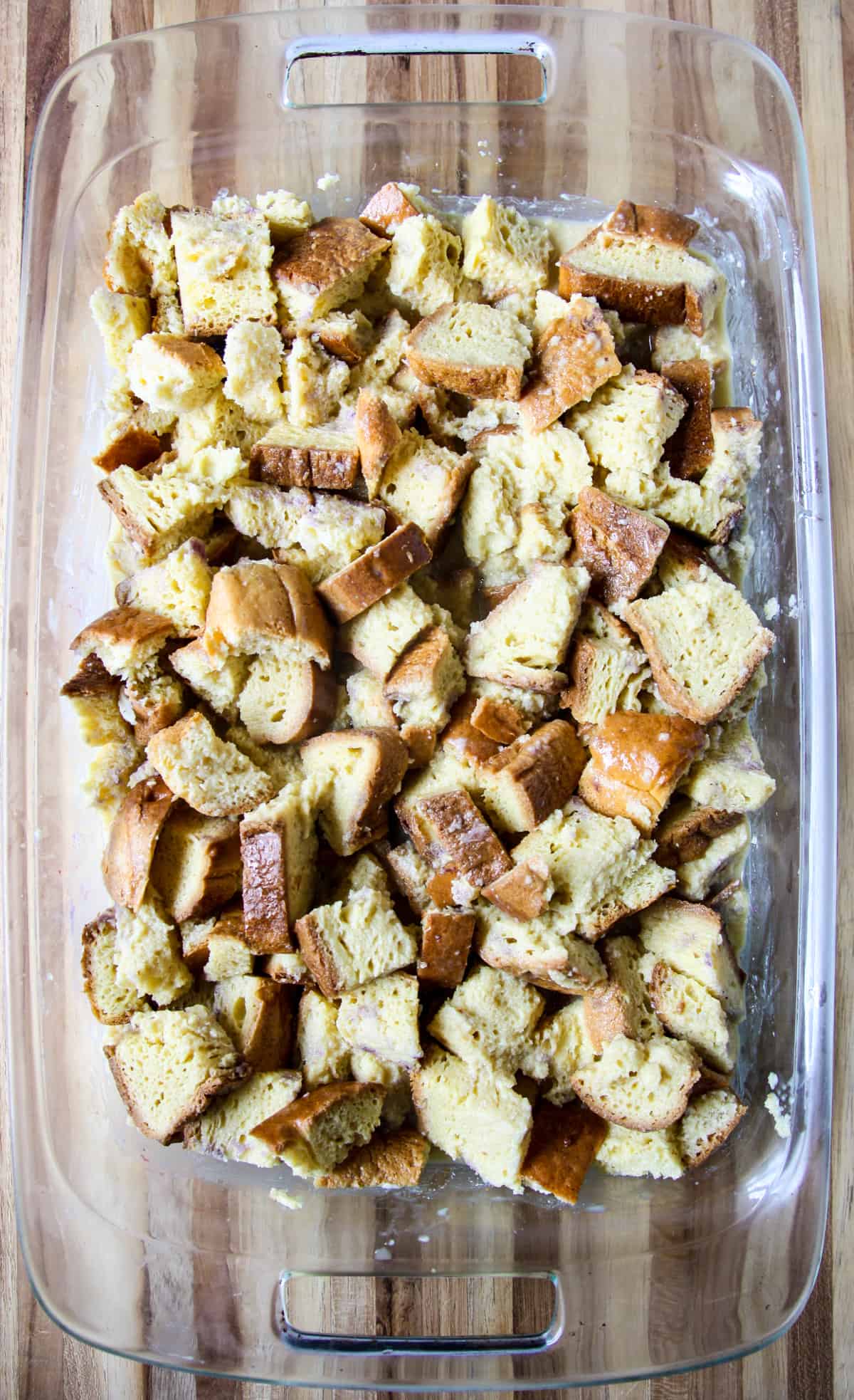 Cubes of bread soaking in custard liquid in a glass baking dish.