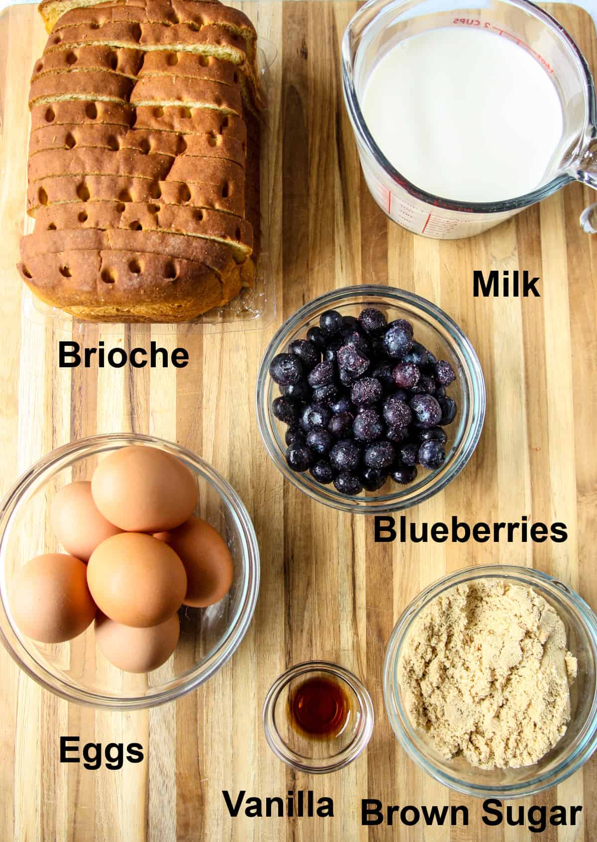 All of the ingredients to make brioche French toast casserole, in glass dishes on a wooden board.