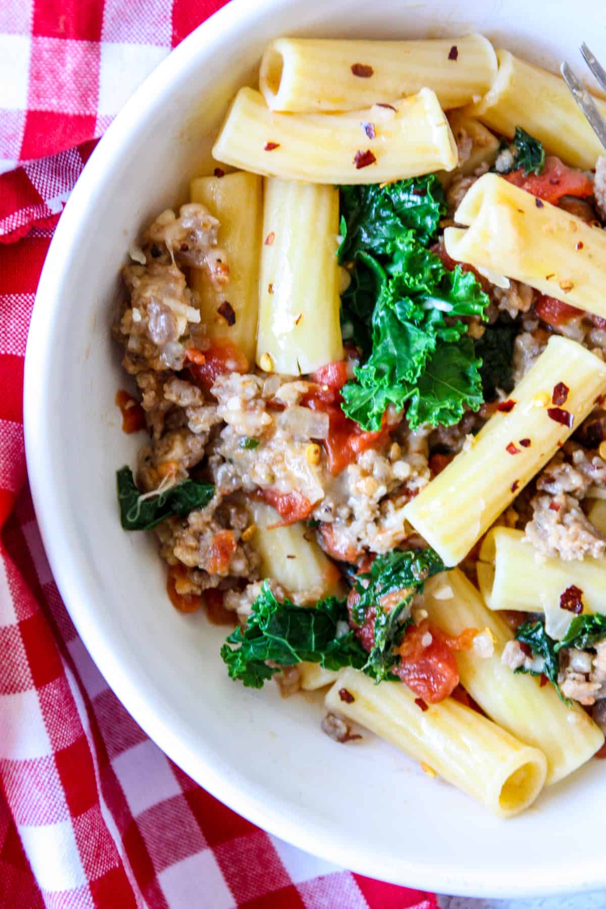 Close up of sausage and kale rigatoni in a white dish.