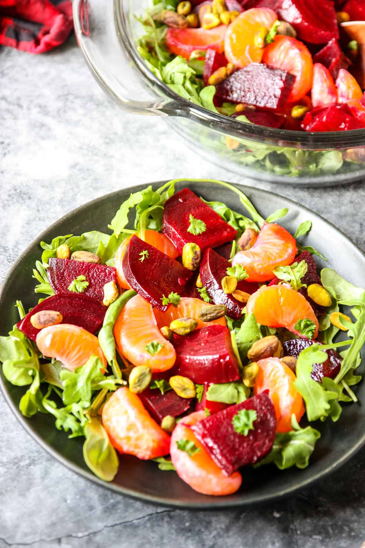 A serving of roasted beet and orange salad on a plate beside the serving bowl.
