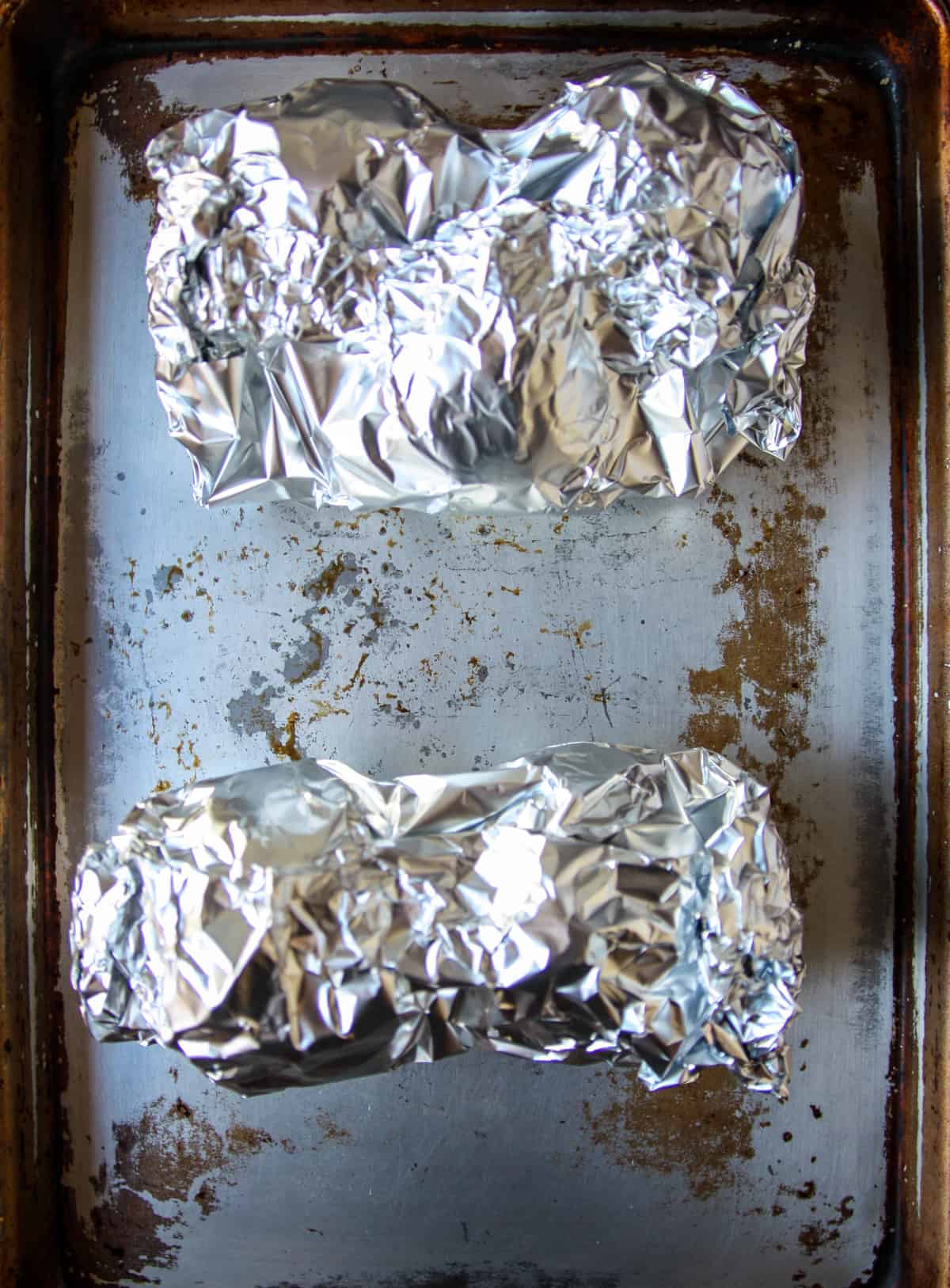 Two packages of beets wrapped in aluminum foil, on a baking sheet.