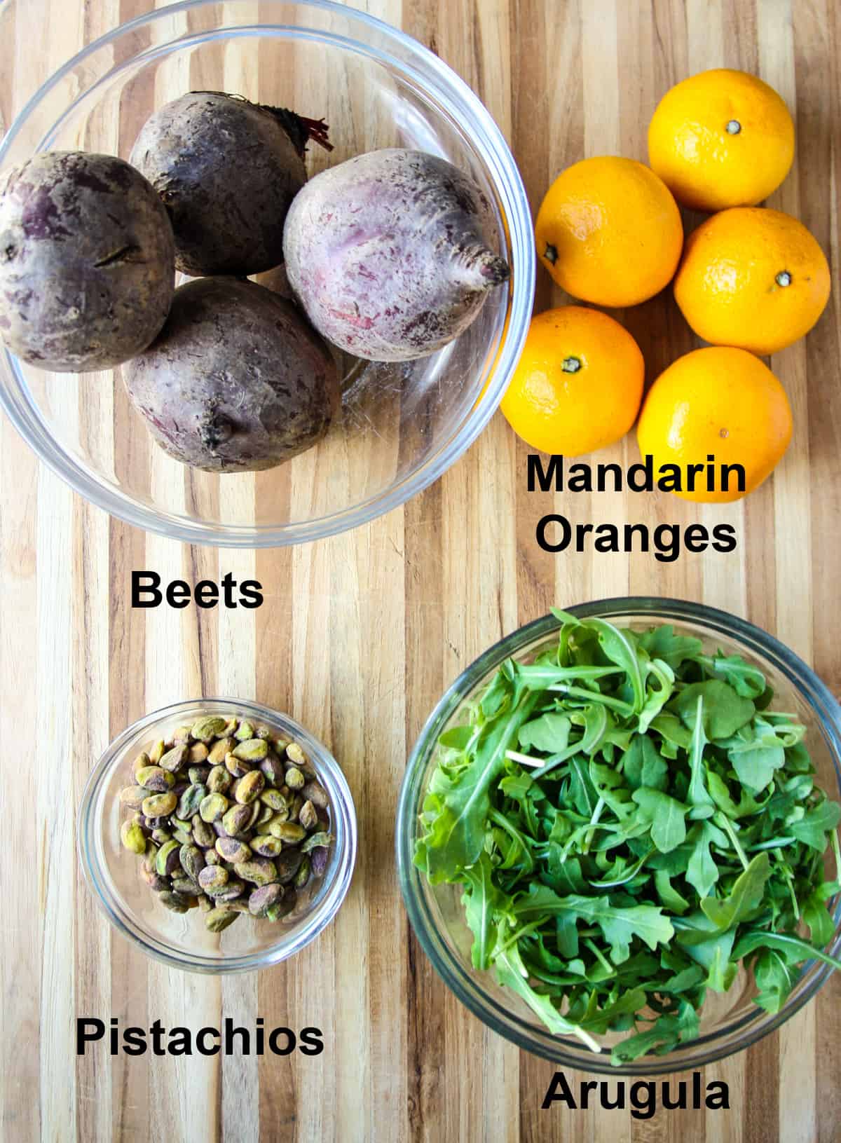 The ingredients for the salad in glass bowls on a wooden board.