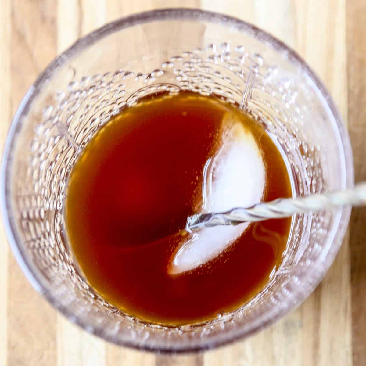 Ice cubes being stirred into a cocktail in a glass.