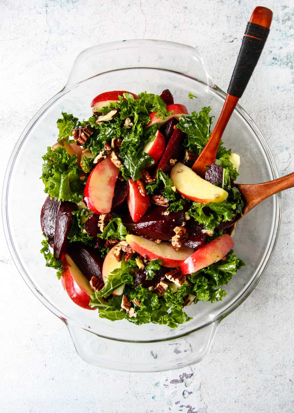 All of the salad ingredients being tossed together in a glass bowl, with two wooden forks.