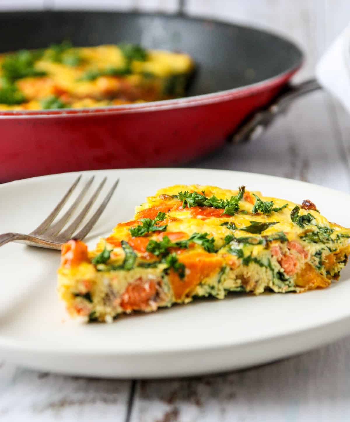 A slice of salmon frittata on a white plate with a silver fork.