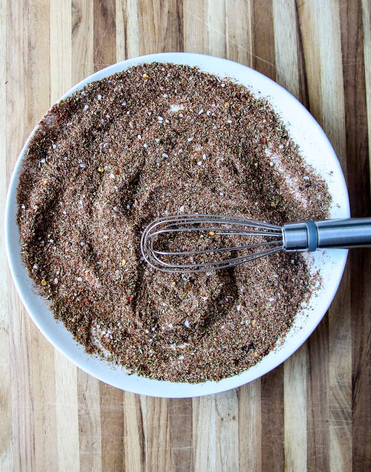Spices combined together on a white plate, with a whisk.