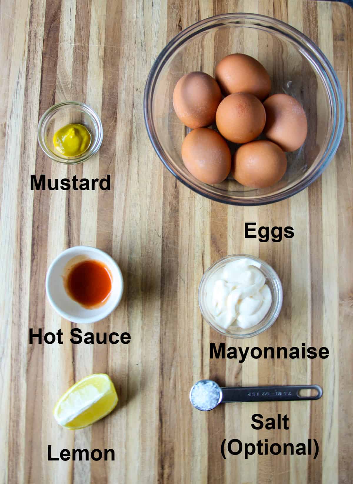 The ingredients for making the deviled eggs, in glass bowls on a wood cutting board.
