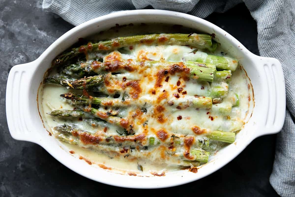 Cheese covered baked asparagus in a casserole dish.