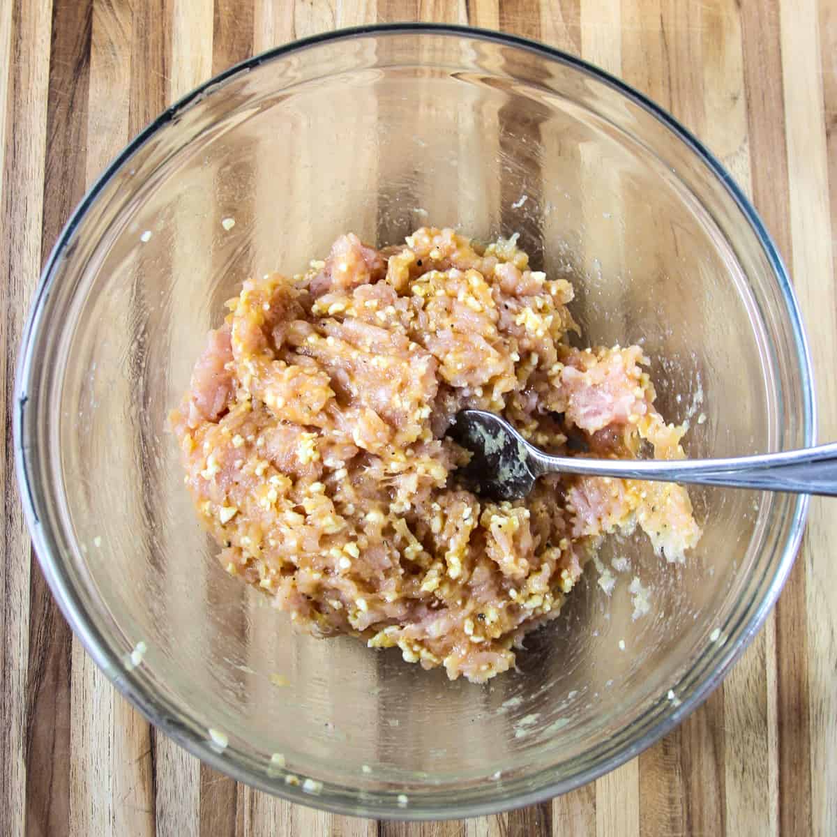 The meatball ingredients being mixed together in a glass bowl.