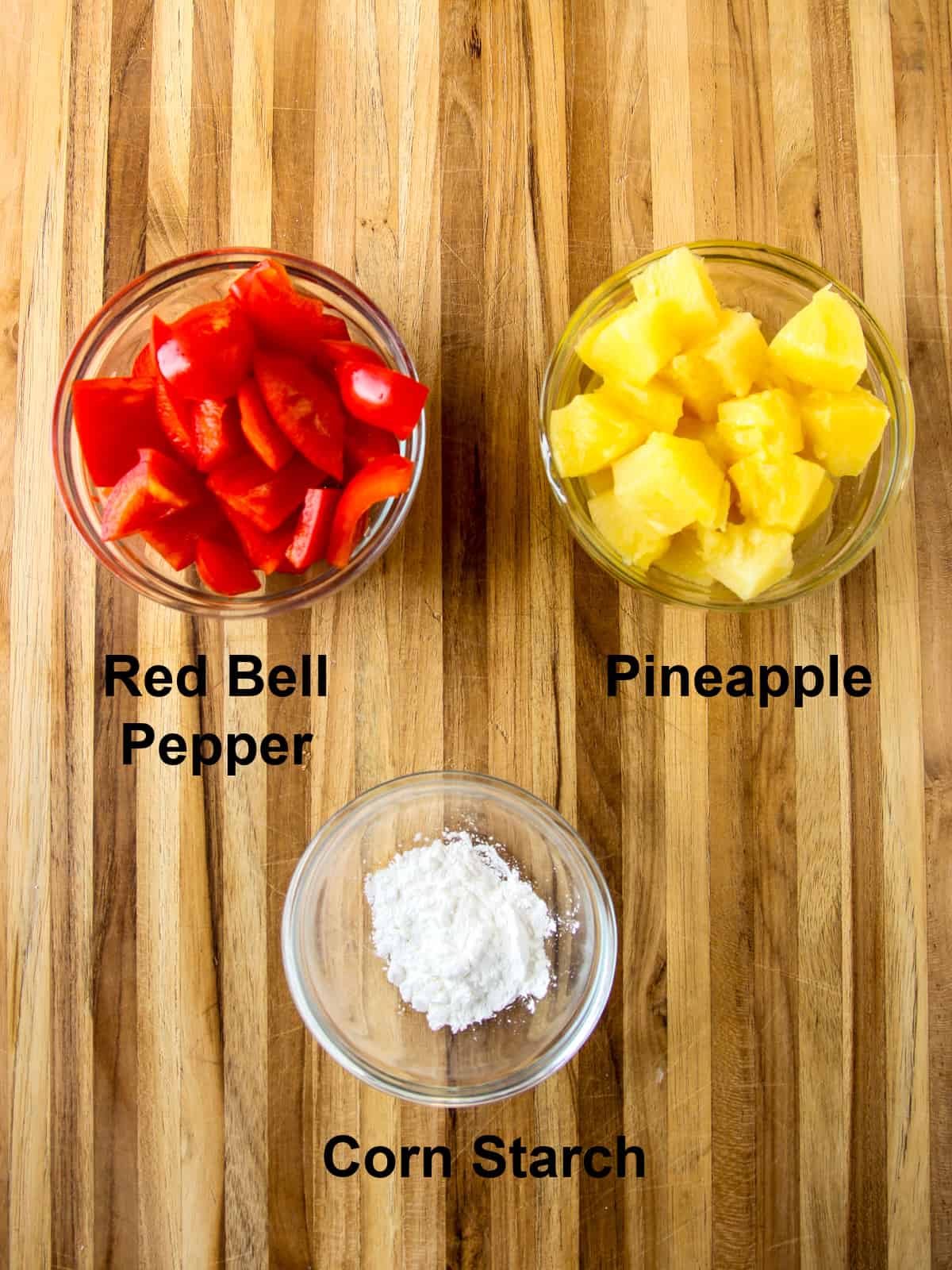 Chopped red bell pepper and pineapple chunks in glass bowls.