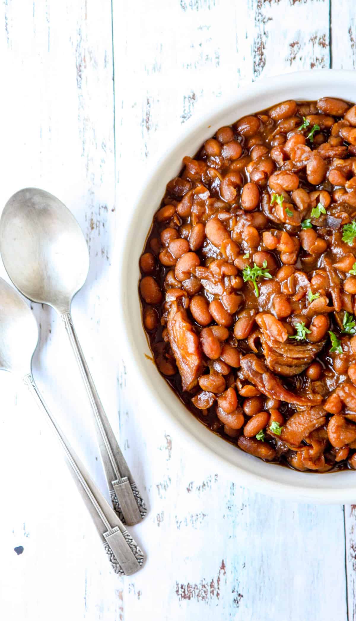 Slow cooker baked beans in a white bowl with a silver spoon.