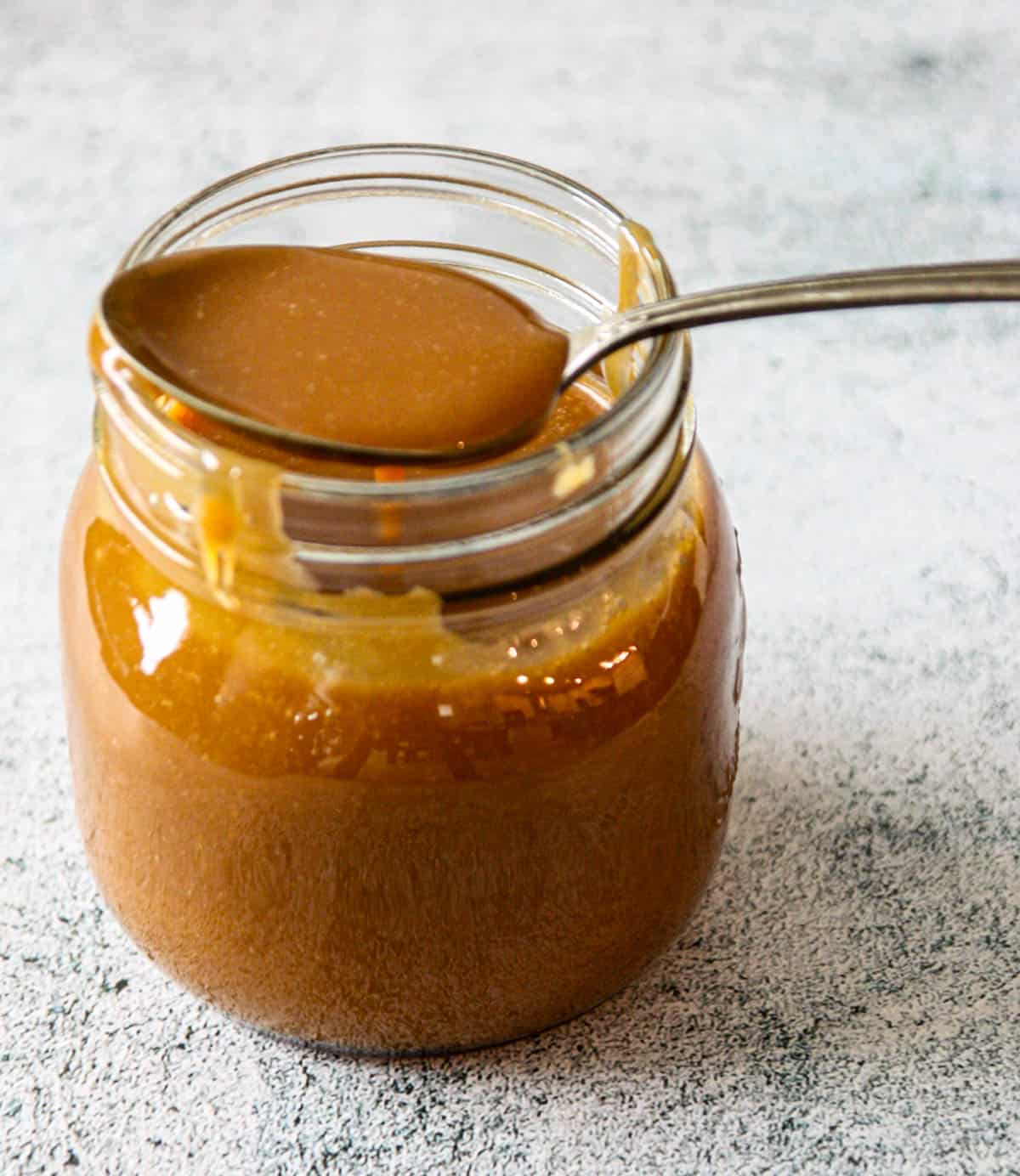 A jar of caramel candy sauce with a silver spoon.