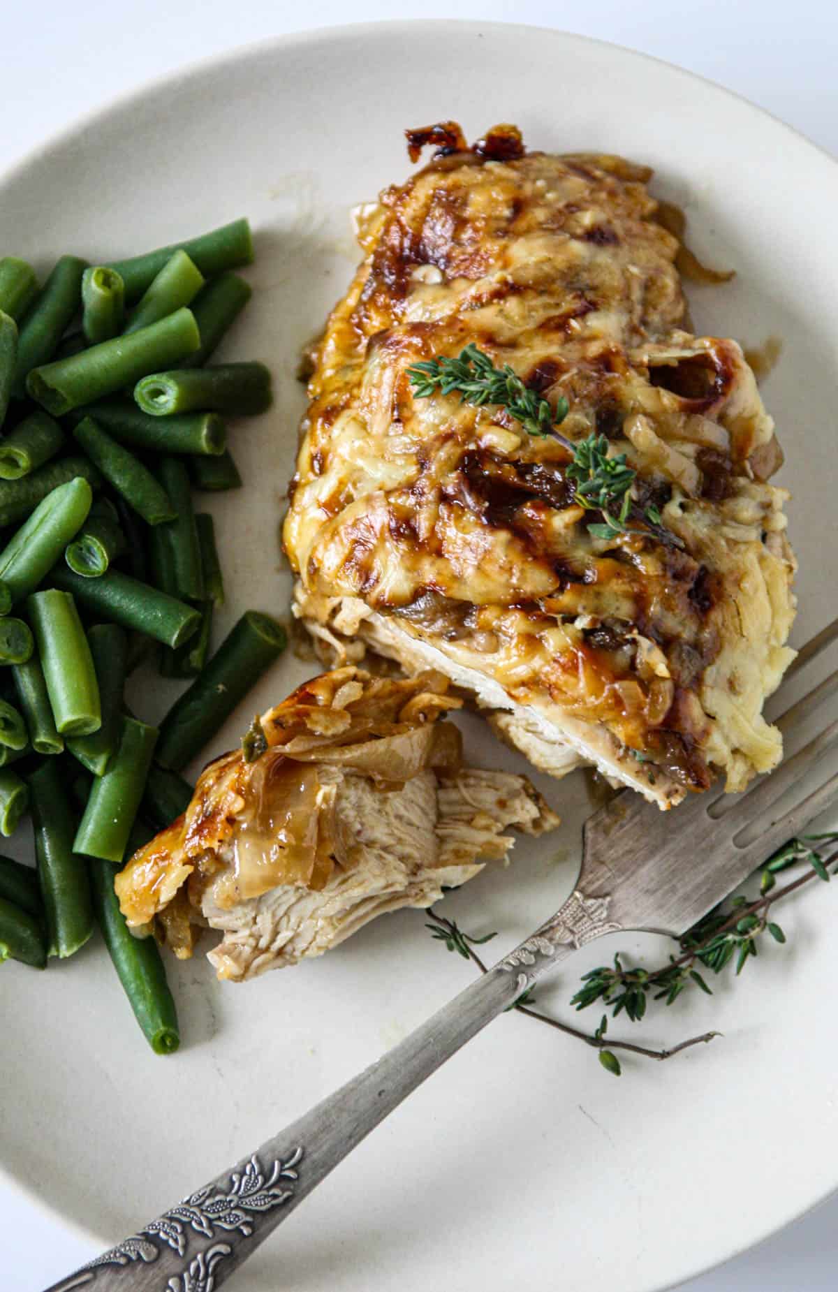 A portion of baked French onion chicken on a white plate with a silver fork.