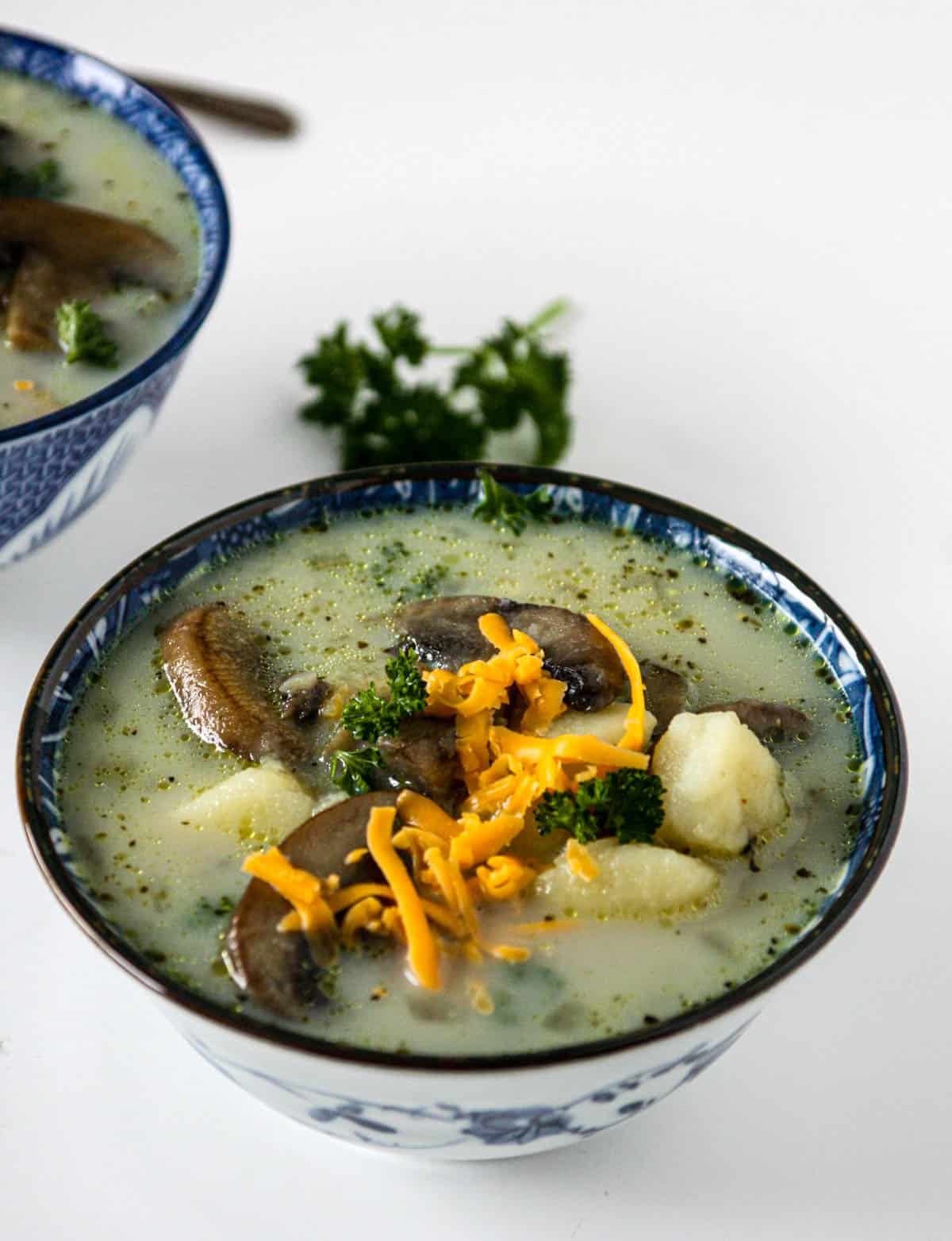 Potato mushroom soup in a blue and white bowl, topped with grated cheese.