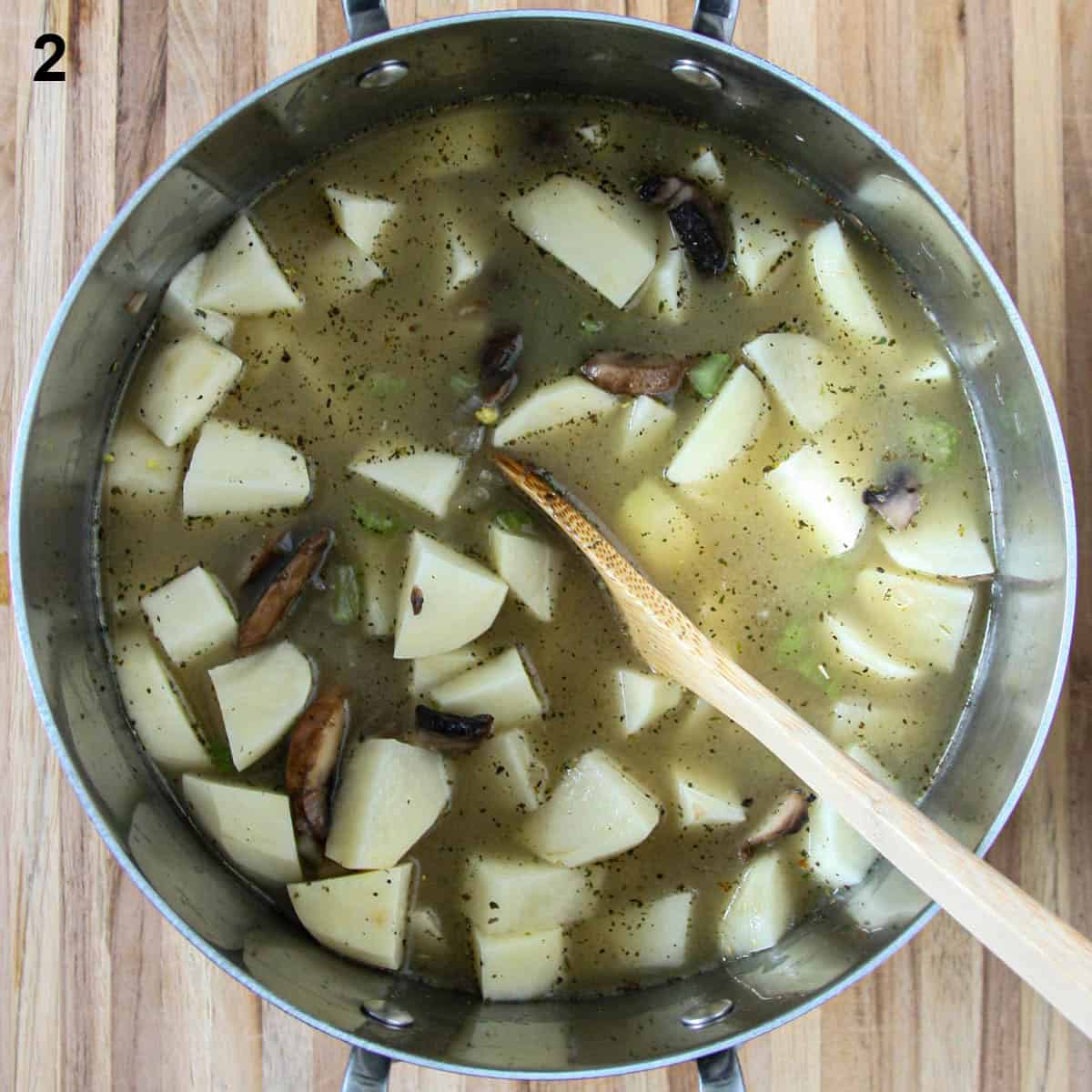 Potatoes and broth in the soup pot being stirred with a wooden spoon.