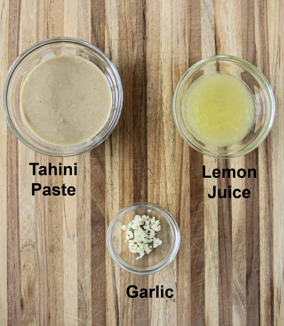 The ingredients for tahini sauce in glass bowls on a wooden board.